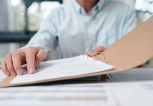 Business professional reviewing documents in a folder at an office desk. Concept of paperwork, administration, contract review, compliance, auditing, and corporate documentation process.