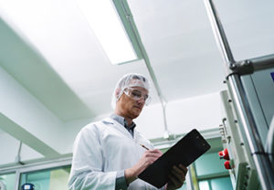 A man in a lab coat is writing on a clipboard. He is wearing a l