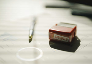 Red approved stamp lying on business documents with charts and graphs waiting for manager approval
