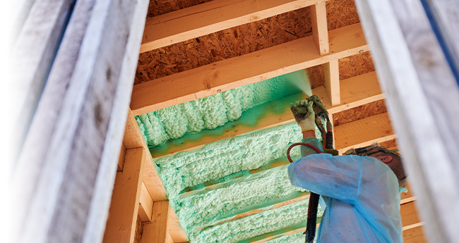 Technician applying spray polyurethane foam insulation between wood roof framing